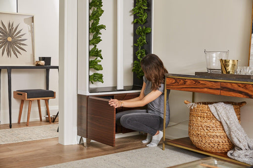 Woman adding nutrients to Oak Aeva indoor garden unit in a living space, featuring leafy green vegetables growing
